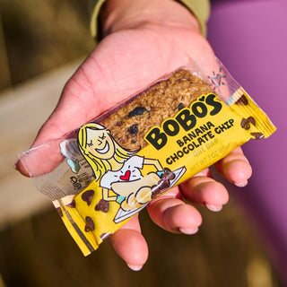 A hand holds a package of Banana Chocolate Chip Oat Bars