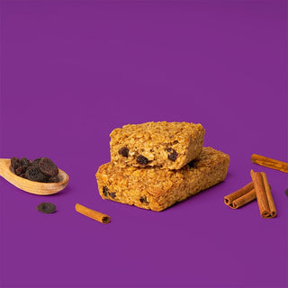 A stack of Cinnamon Raisin Oat Bars with raisins, cinnamon sticks, and a bowl of raisins. 