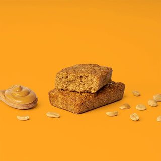 A close-up of a Peanut Butter Oat Bar, featuring a stack of oatmeal bars, a cookie, and a peanut butter spread on a spoon. 