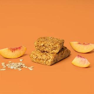 A peach oat bar surrounded by oats, showcasing a slice of peach with a bite taken out. 
