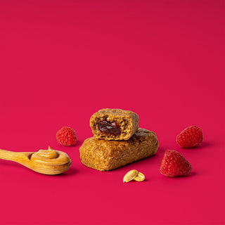 Oat bar on pink background with surrounding peanuts and raspberries
