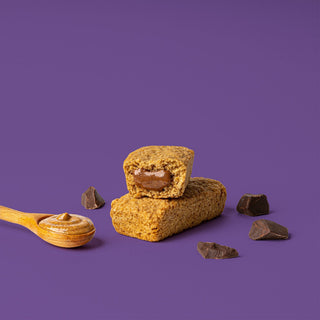 Oat bar on purple background with surrounding chocolate chunks and almond butter