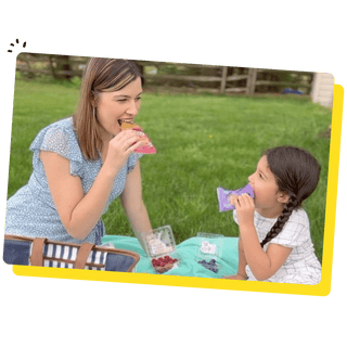 Image of an adult and a child eating Bobo's together on a picnic blanket