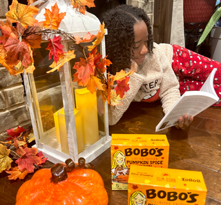 Image of a child reading a book next to two boxes of Bobo's Pumpkin Spice Oat Bars